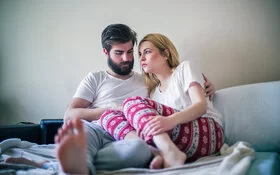 Ein junges Paar mit unerfülltem Kinderwunsch sitzt auf dem Bett und ist betrübt.