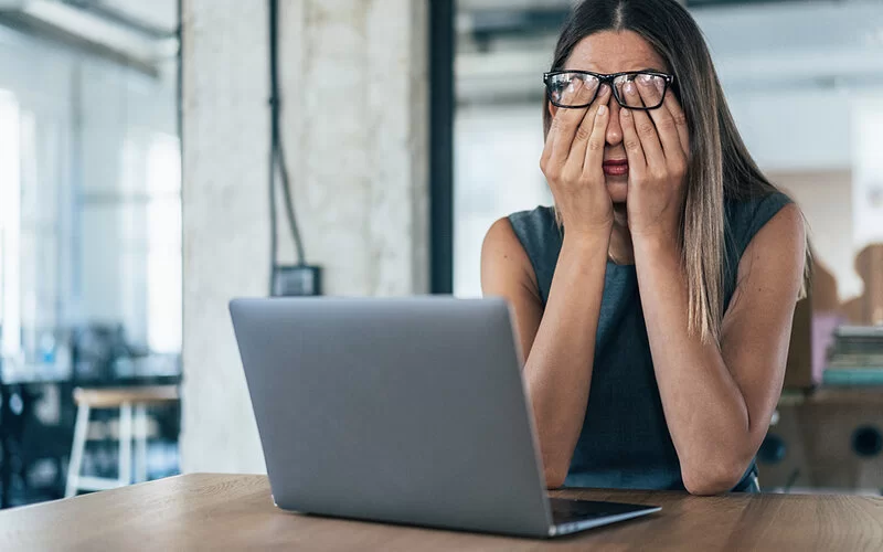 Frau sitzt vor ihrem Laptop und reibt sich müde die Augen, weil sie nicht gut geschlafen hat.