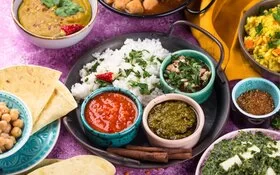 Indisches Chutney in kleinen Gefäßen serviert mit Reis und Brot auf einem Teller.