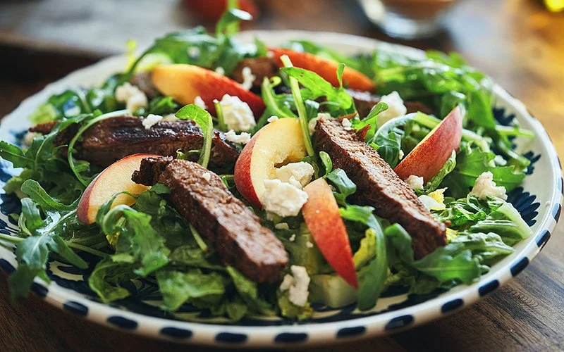 Rucola-Salat mit gebratenem Steak und Pfirsichen, angerichtet auf einem Teller.