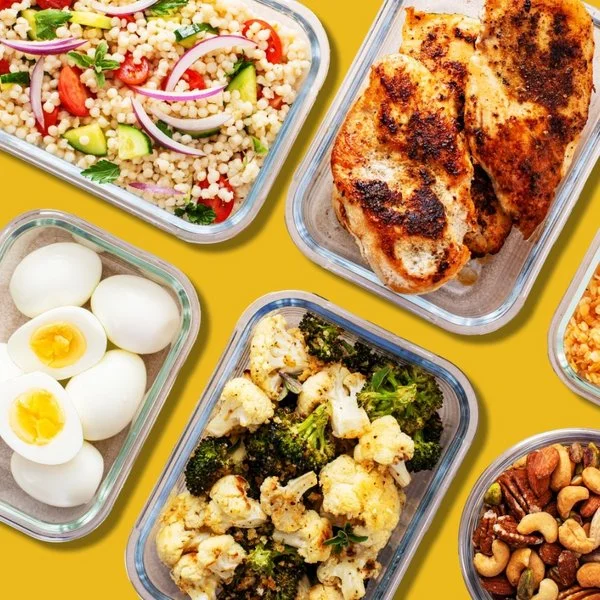 Mehrere Glasbehälter mit gekochtem Gemüse, gebratenem Fleisch, Eiern, Nüssen und Salat auf gelbem Hintergrund.