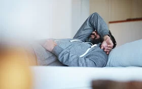 Mann mit psychosomatischen Beschwerden liegt auf der Couch.