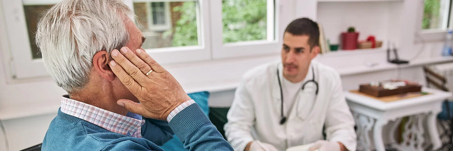 Ein älterer Mann im Rollstuhl sitzend erklärt seinem Arzt seine Hörprobleme.