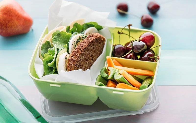 Eine gefüllte Brotbox mit Sandwich, Gemüse und Kirschen.