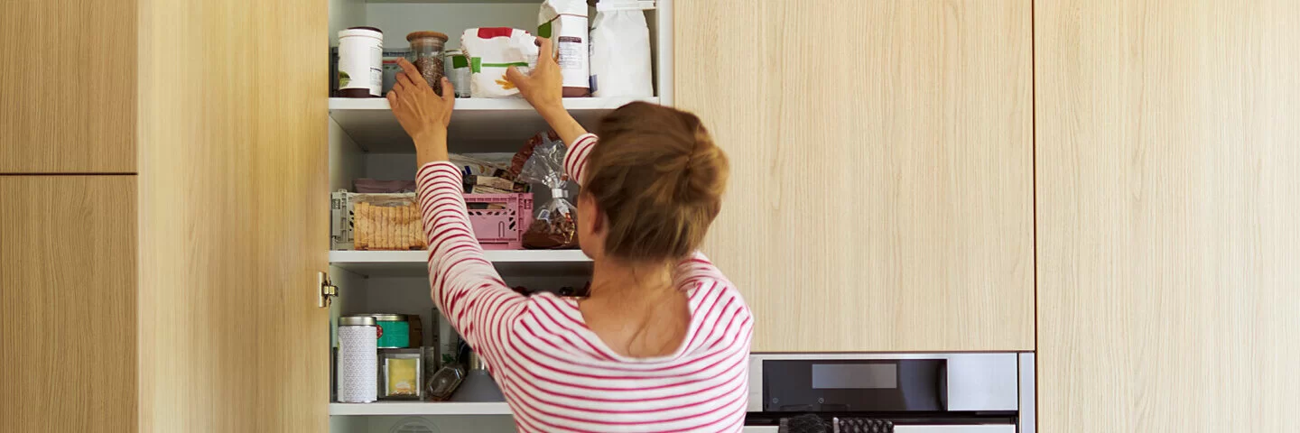 Junge Frau räumt ihre Küchenschränke auf.