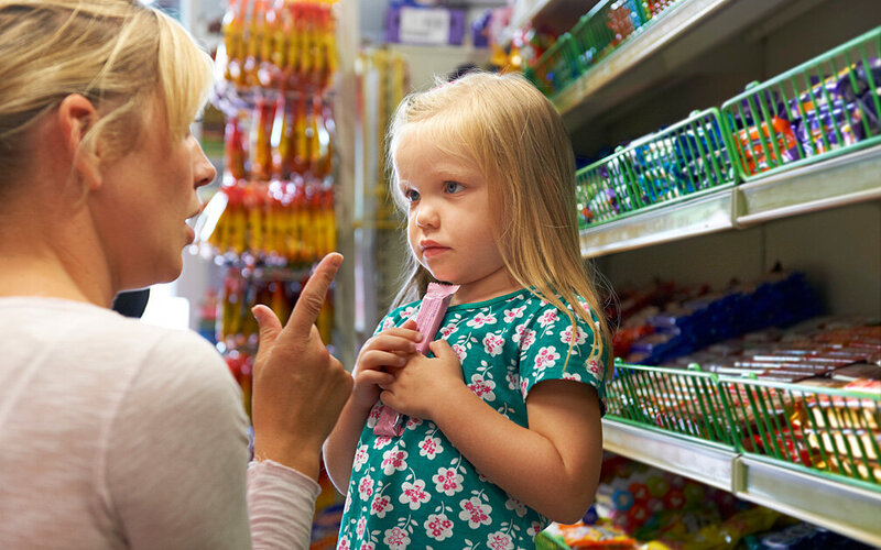 Mutter verbietet ihrer kleinen Tochter im Supermarkt Süßigkeiten, da diese eine gesunde Ernährung für Kleinkinder nicht fördern.
