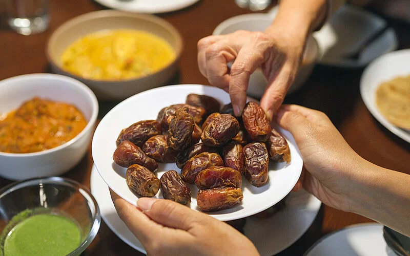 Zum Iftar oder Fastenbrechen werden Datteln auf einem Teller gereicht, mehrere Menschen greifen zu.