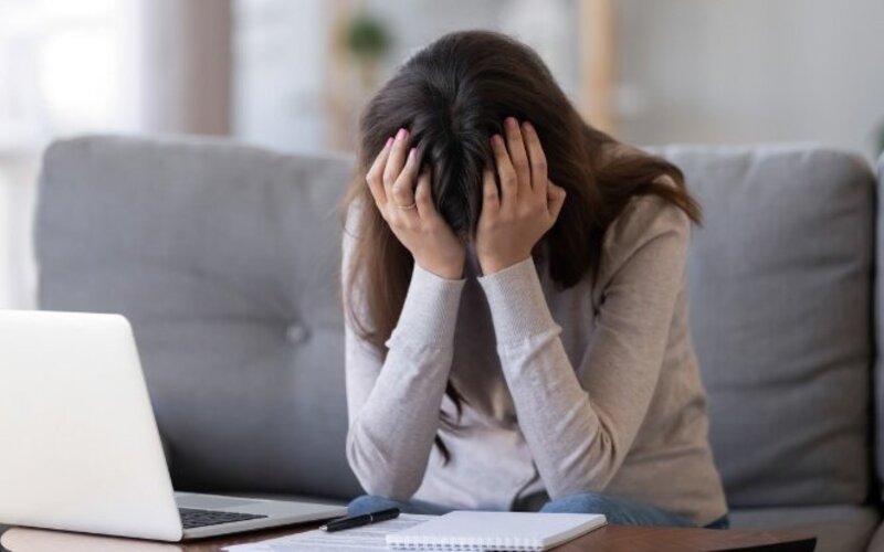 Junge Frau sitzt vor dem Laptop und hat den Kopf in den Händen.