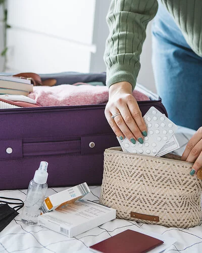 Eine Frau packt Tabletten in eine Kosmetiktasche. Daneben liegt ein geöffneter Koffer auf dem Bett.