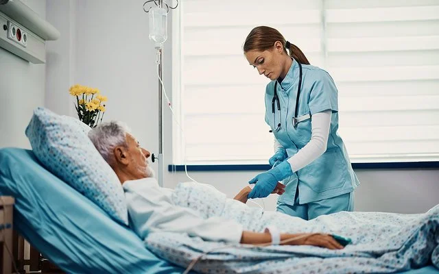 Eine Gesundheits- und Krankenpflegerin bereitet eine Infusion für einen älteren Patienten vor, der im Bett liegt.