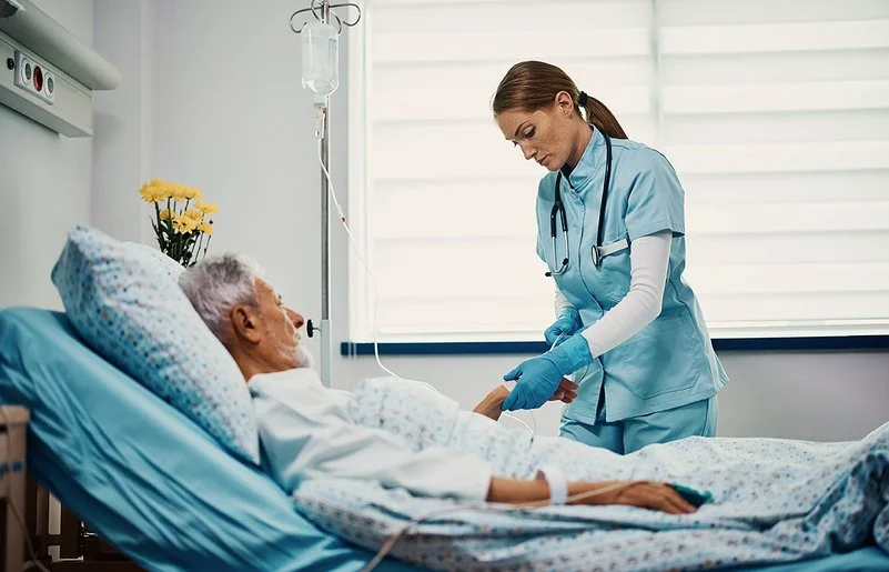 Eine Gesundheits- und Krankenpflegerin bereitet eine Infusion für einen älteren Patienten vor, der im Bett liegt.