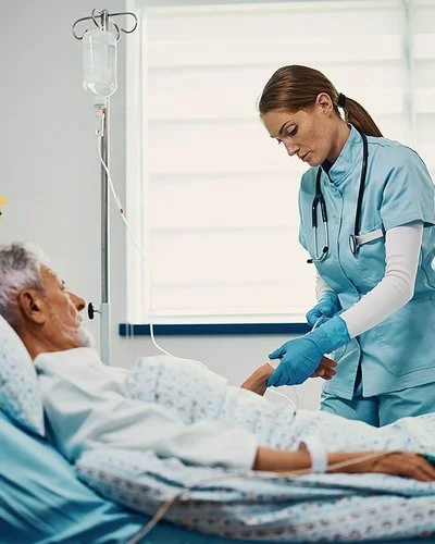 Eine Gesundheits- und Krankenpflegerin bereitet eine Infusion für einen älteren Patienten vor, der im Bett liegt.