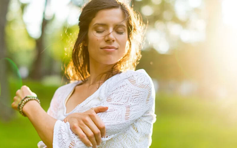 Frau steht in der freien Natur und führt Qigong-Übungen durch