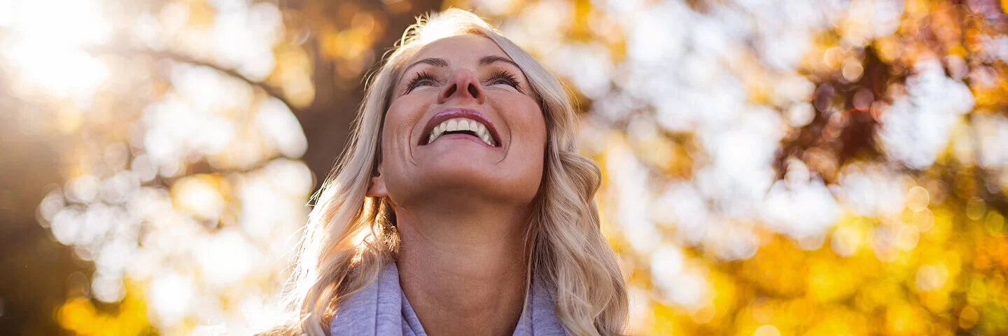 Eine Frau mit Diabetes, die in den Wechseljahren ist, geht im Park spazieren und schaut in die Baumkronen.