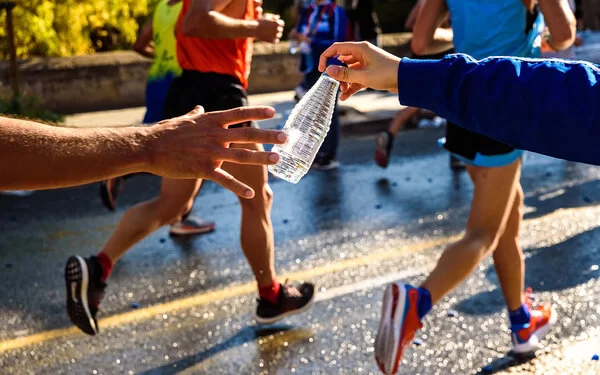 Ein Mensch reicht einem Marathonläufer eine Flasche Wasser.