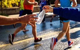 Ein Mensch reicht einem Marathonläufer eine Flasche Wasser.