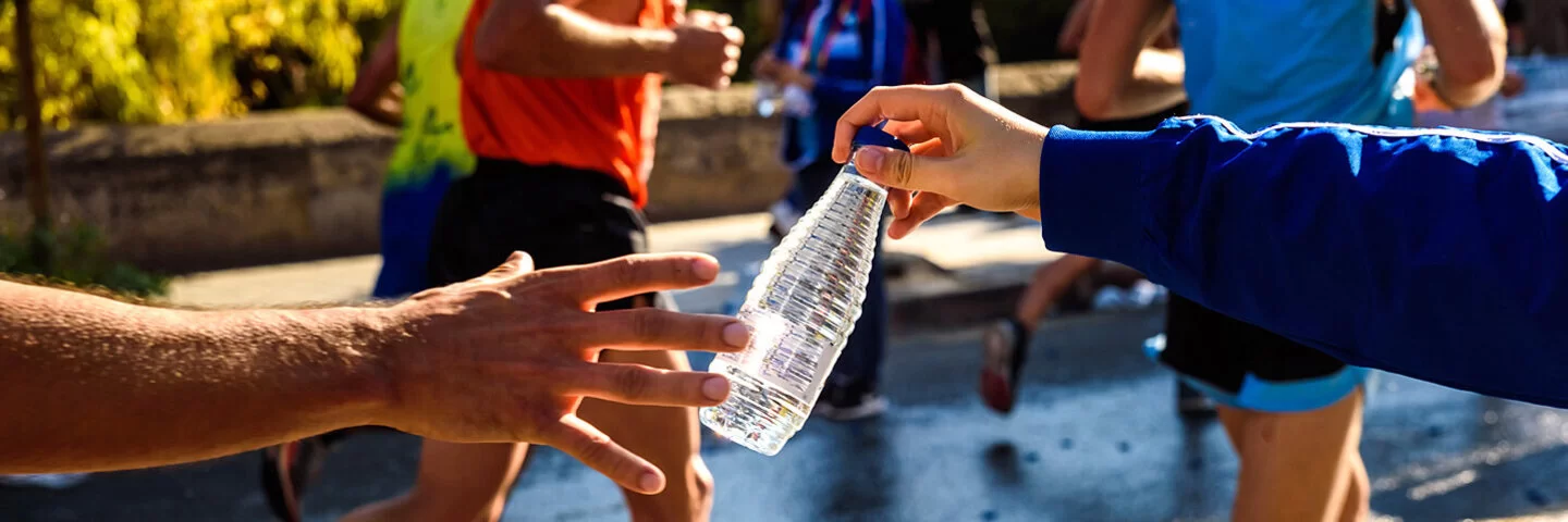 Ein Mensch reicht einem Marathonläufer eine Flasche Wasser.