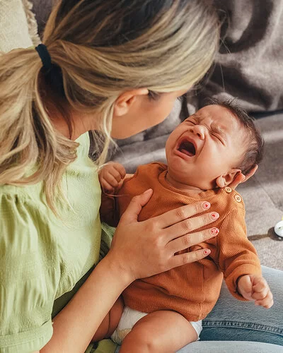 Eine junge Mutter versucht ihr schreiendes Neugeborenes, das auf ihrem Schoß liegt, zu beruhigen.