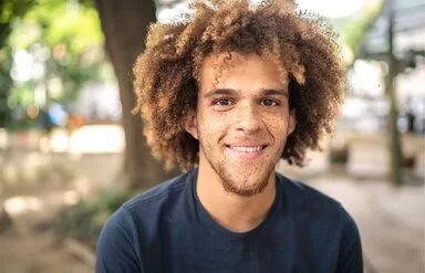 Ein junger Mann mit Sommersprossen im Gesicht lächelt in die Kamera.