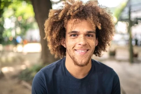 Ein junger Mann mit Sommersprossen im Gesicht lächelt in die Kamera.