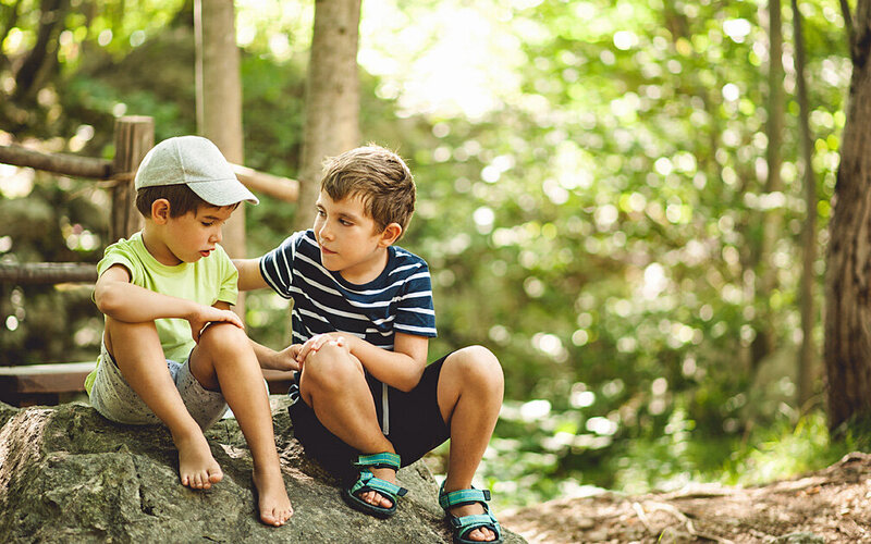 Zwei Jungen sitzen am Waldrand, der große tröstet den kleinen.