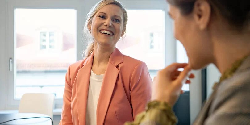 Zwei gut gelaunte Frauen sprechen miteinander. Als Berufseinsteigerinnen sind sie bei der AOK gut versichert.
