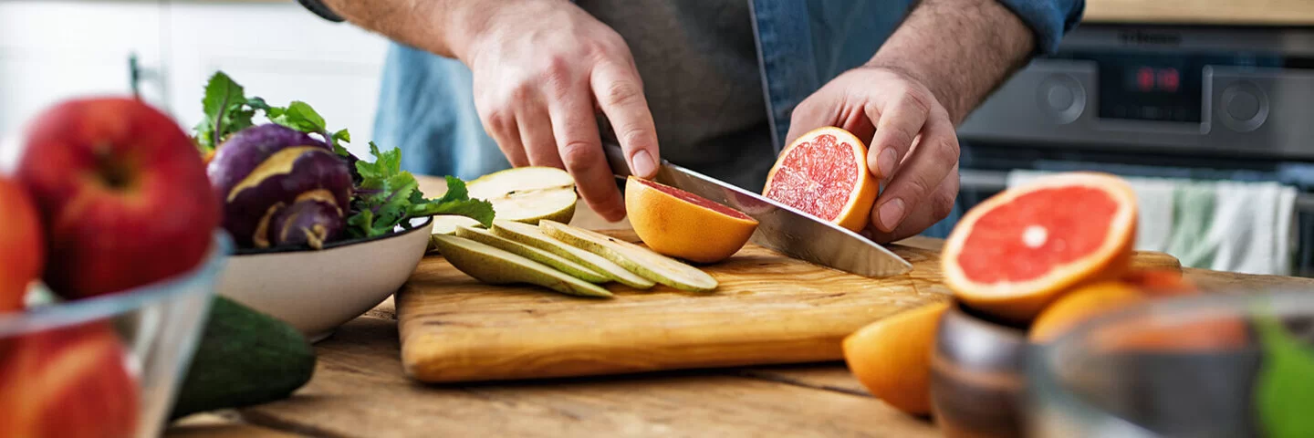 Ein Mann schneidet Obst: Auf dem Schneidebrett liegen Obstsorten wie Grapefruit und Birne, die bei Diabetes geeignet sind.