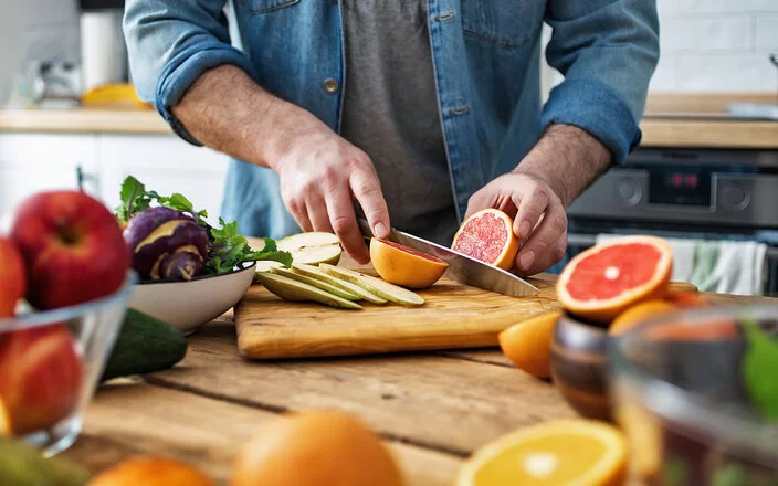 Ein Mann schneidet Obst: Auf dem Schneidebrett liegen Obstsorten wie Grapefruit und Birne, die bei Diabetes geeignet sind.