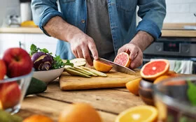 Ein Mann schneidet Obst: Auf dem Schneidebrett liegen Obstsorten wie Grapefruit und Birne, die bei Diabetes geeignet sind.