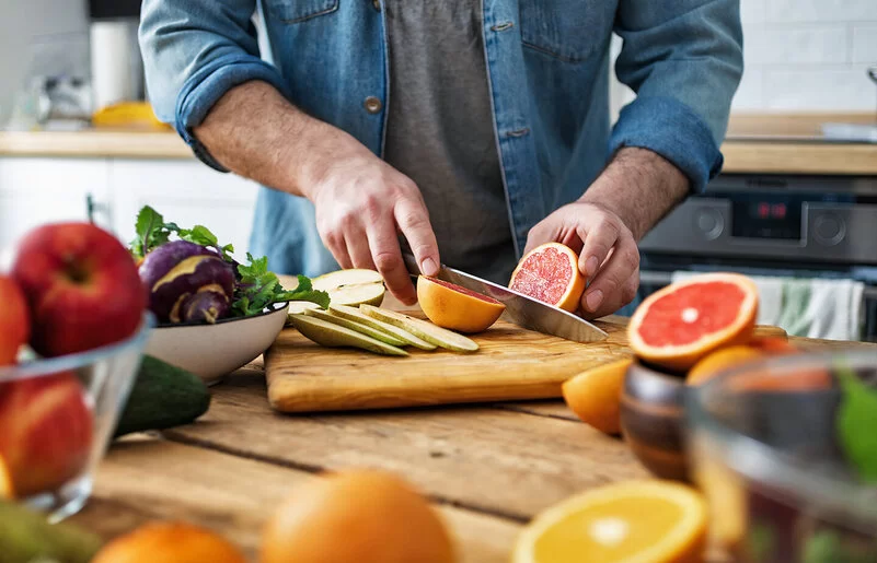 Ein Mann schneidet Obst: Auf dem Schneidebrett liegen Obstsorten wie Grapefruit und Birne, die bei Diabetes geeignet sind.