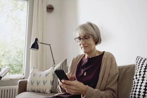 Ältere Dame sitzt auf dem Sofa und schaut auf ihr Smartphone