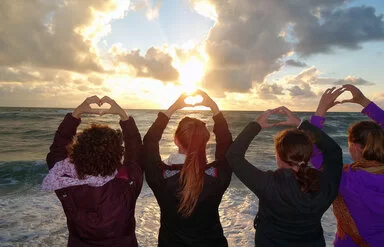 Vier Jungendliche stehen an einem Strand und schauen der Sonne entgegen, während sie mit den H�änden Herzen formen.