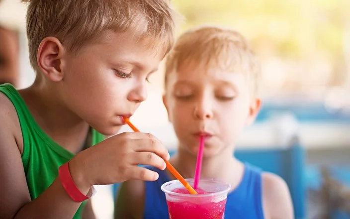 Zwei Kinder in sommerlicher Kleidung trinken mit Strohhalmen aus einem Slush-Eis-Becher.