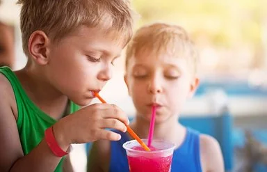 Zwei Kinder in sommerlicher Kleidung trinken mit Strohhalmen aus einem Slush-Eis-Becher.