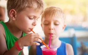 Zwei Kinder in sommerlicher Kleidung trinken mit Strohhalmen aus einem Slush-Eis-Becher.