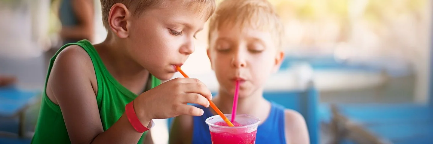 Zwei Kinder in sommerlicher Kleidung trinken mit Strohhalmen aus einem Slush-Eis-Becher.