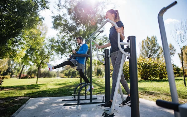 Ein junger Mann und eine junge Frau in Sportkleidung trainieren in einem Park an Fitnessgeräten.