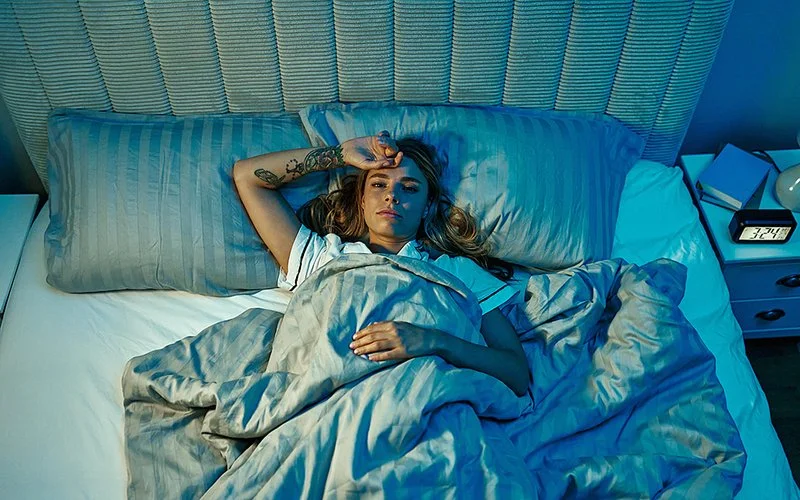 Im abgedunkelten Schlafzimmer liegt eine Frau im Bett. Ihre Augen sind geöffnet.