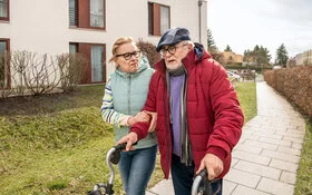 Mann mit Gehhilfe (Rollator) geht mit seiner Frau spazieren.