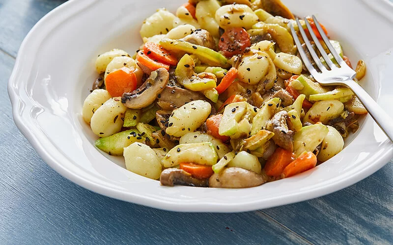 In einem Teller sind Gnocchi mit frischem Gemüse angerichtet, zum Beispiel mit Möhren und Pilzen.