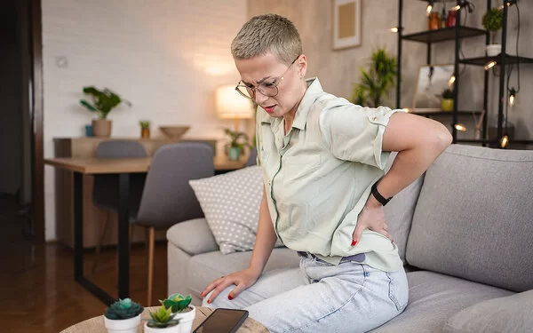 Eine Frau sitzt auf einem Sofa und hält sich mit einer Hand den Rücken.