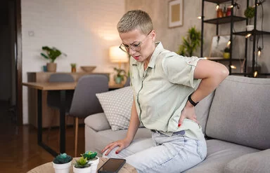 Eine Frau sitzt auf einem Sofa und hält sich mit einer Hand den Rücken.