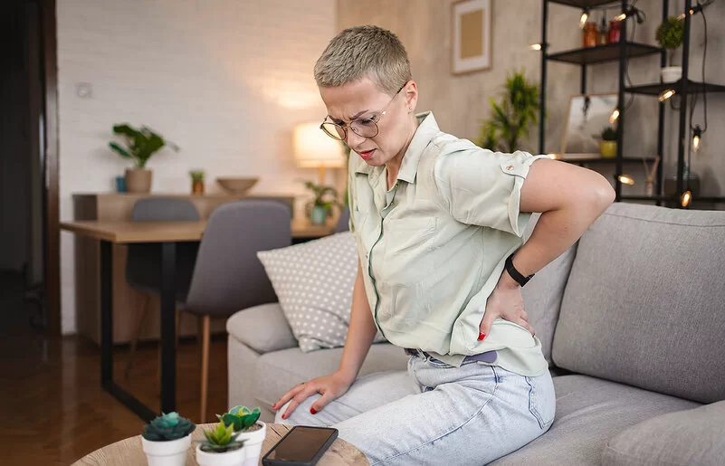 Eine Frau sitzt auf einem Sofa und hält sich mit einer Hand den Rücken.
