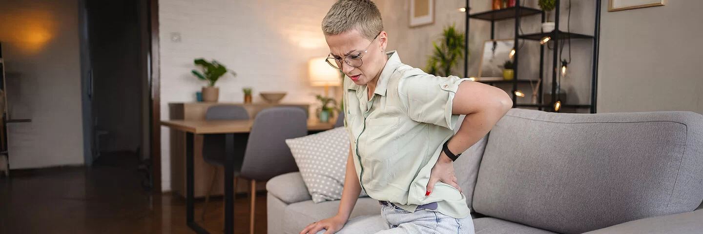 Eine Frau sitzt auf einem Sofa und hält sich mit einer Hand den Rücken.