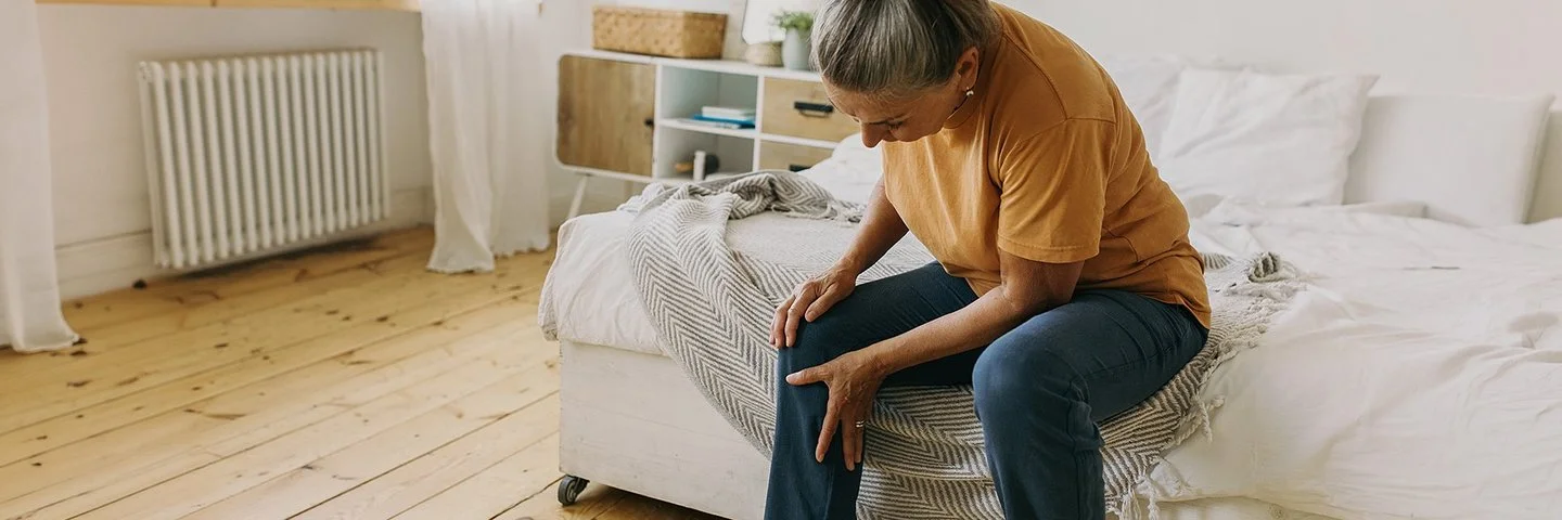 Eine Frau sitzt auf einem Bett und hält sich das Knie.