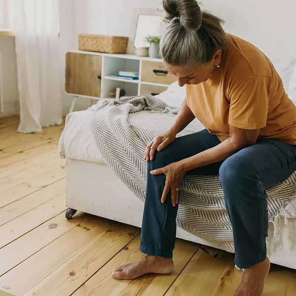 Eine Frau sitzt auf einem Bett und hält sich das Knie.
