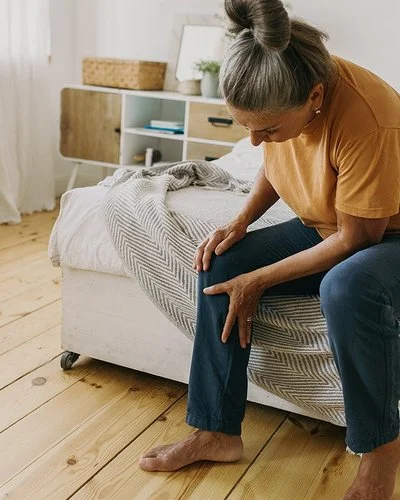 Eine Frau sitzt auf einem Bett und hält sich das Knie.