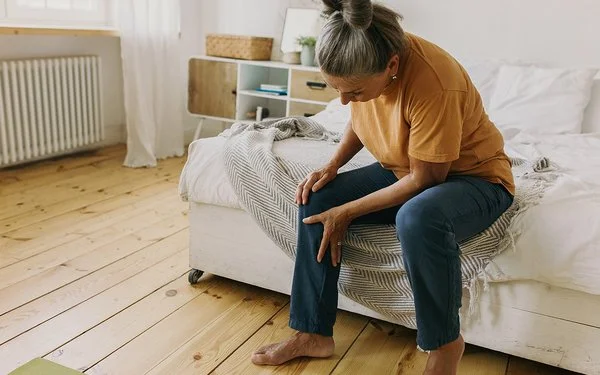 Eine Frau sitzt auf einem Bett und hält sich das Knie.