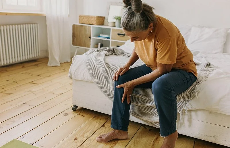 Eine Frau sitzt auf einem Bett und hält sich das Knie.