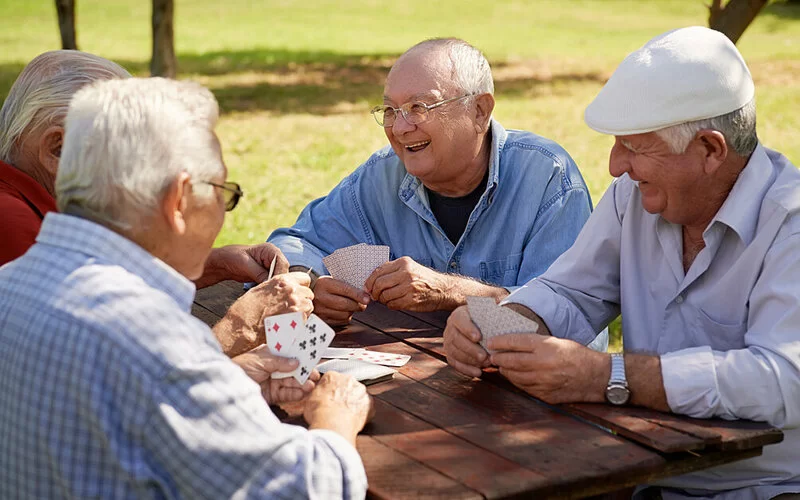 Vier ältere Männer sitzen an einem Tisch im Park und spielen Karten.